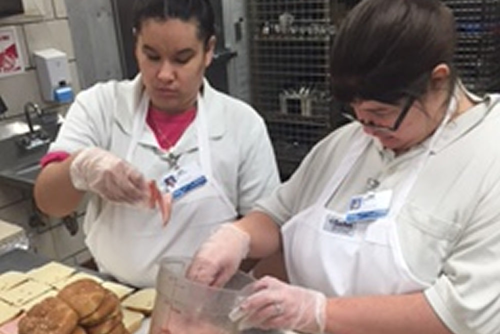 Students wearing personal protective equipment preparing food in Henry Ford Hospital's kitchen.